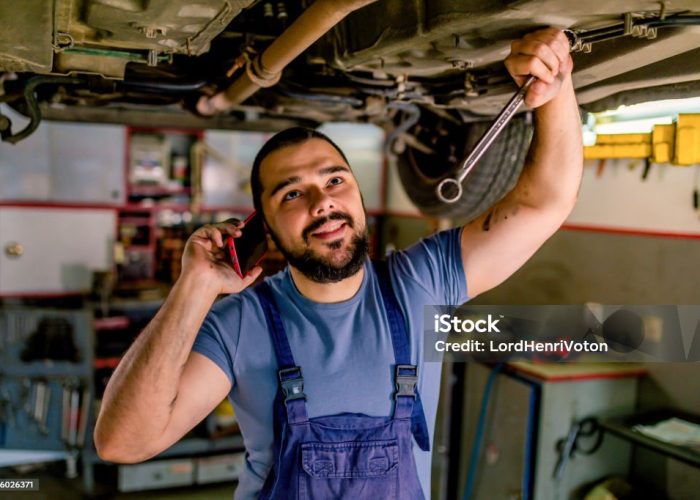 Young auto mechanic talking on cell phone in a workshop