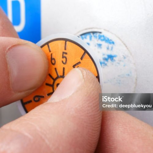 TÜV successfully passed, Hand of TÜV agent sticks new TÜV seal on motorcycle plate. The motorcycle passed the test. Tüv badge is stuck on car number plate, TÜV official sticks new TÜV badge on car number plate